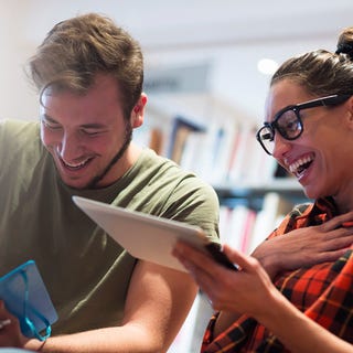 Two students talking and laughing while holding a tablet and learning a language with Berlitz Nicaragua's online classes