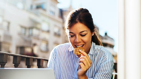 Woman on a balcony eating a cookie and learning a language online with Berlitz Nicaragua on her laptop