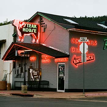 An exterior view of Rod’s Steak House in Williams, Arizona. The restaurant looks like a large house, and it is lit up by several colorful neon signs attracting visitors to come dine.