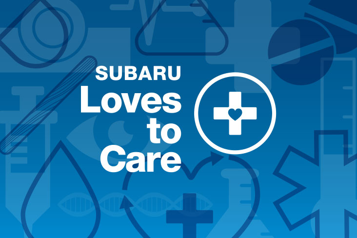 Subaru Loves to Care logo in white lettering on a blue background. To the right of the words “Subaru Loves to Care” is an illustration of a cross with a heart in the center, and it is enclosed in a circle.