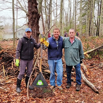 Jack Frost is on the far left and next to him are two leaders from Stanley Subaru. They are outdoors and holding rakes for the Earth Day cleanup work at Woodlawn Museum and public garden.