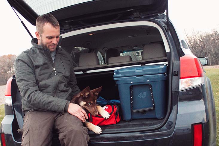 Man and dog in the trunk of car next to first aid kit bags and storage