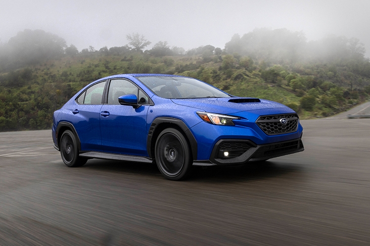 The side profile of a sleek 2022 Subaru WRX driving at a high speed with fog-covered trees in the distance.