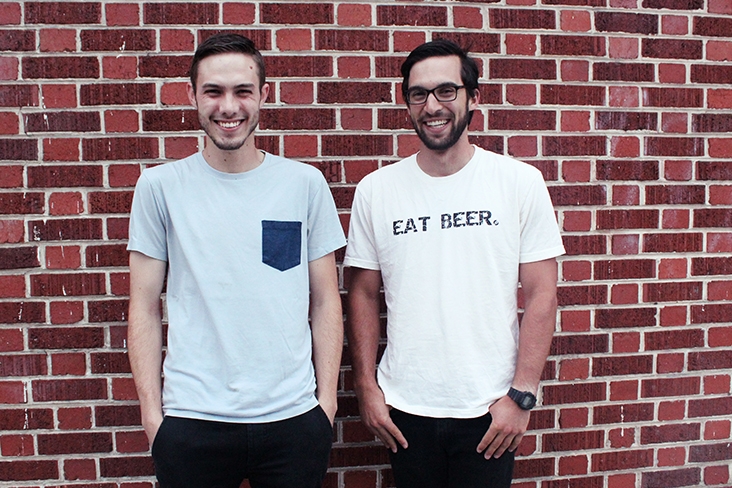 ReGrained co-founders Jordan Schwartz and Dan Kurzrock are standing side by side in front of a brick wall, smiling. Kurzrock is wearing a T-shirt that says, “Eat Beer.”