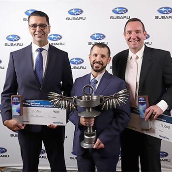 The top three Zone Champion competitors are standing in front of a wall with the Subaru logo peppered across it. They are wearing suits and holding their prizes, which include large checks and a trophy. From left to right are Rolando Ramirez, James Pedicone and Christopher Raymond.