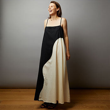 A studio shot of Julia Bainbridge laughing. She’s wearing a floor-length, two-tone dress in black and white. Behind her, the backdrop is gray.