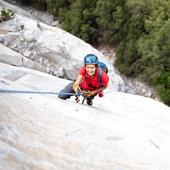 Dierdre Wolownick wearing a helmet and holding onto a rope while climbing up a rockface.