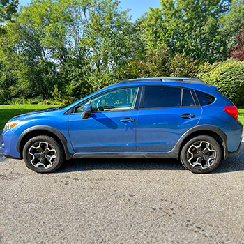 Sauter's 2015 Subaru Crosstrek parked on the street with deciduous trees with green leaves in the distance.