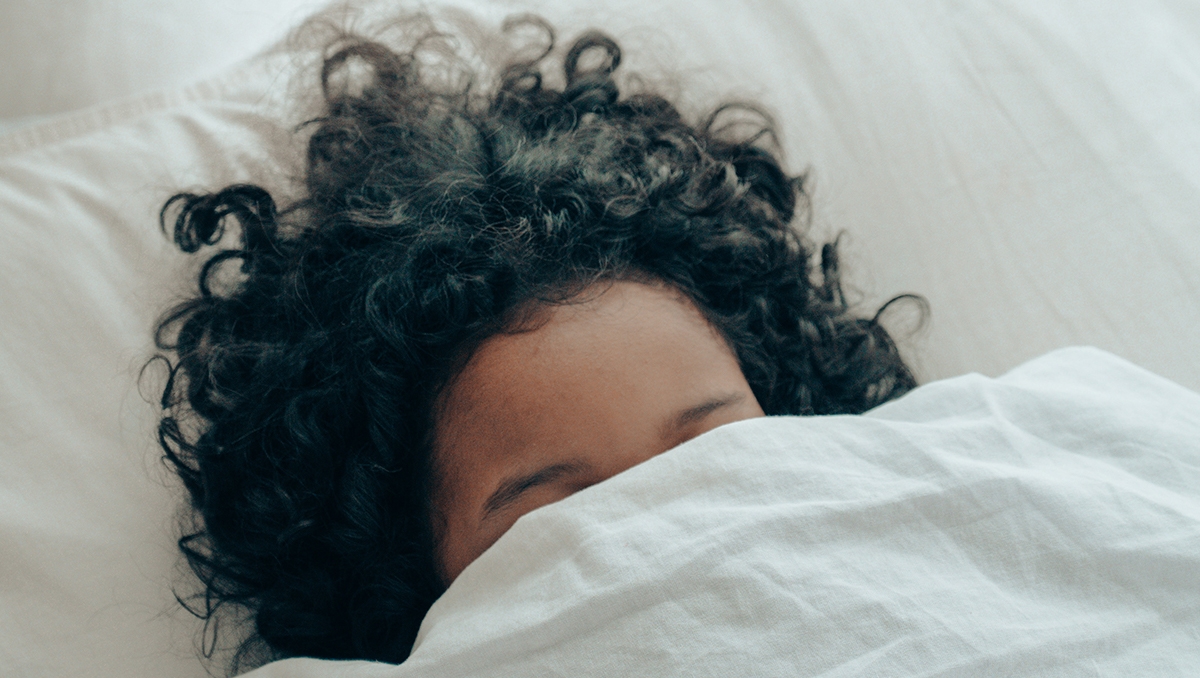 A woman sleeping with her covers pulled up over her face.