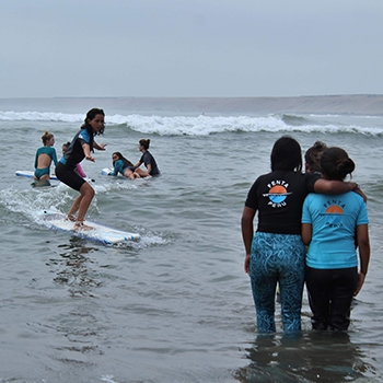 students watch as surfing student rides a wave into shore