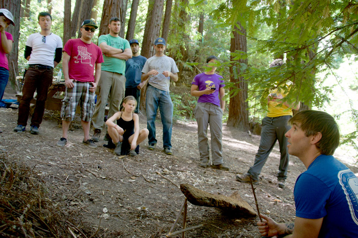 A small group of people are in a forest listening to an instructor. 