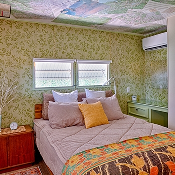 A light-filled bedroom with maps on the ceiling and space to set out belongings on a desk and side table.