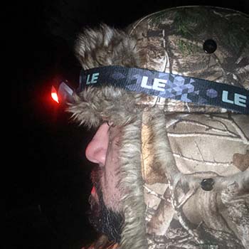 Close-up of a bearded man wearing the LE LED headlamp on his forehead over the hood of a beige parka.