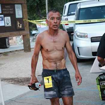Ruperto Romero wearing shorts, no shirt and carrying a bottle of water during a race.