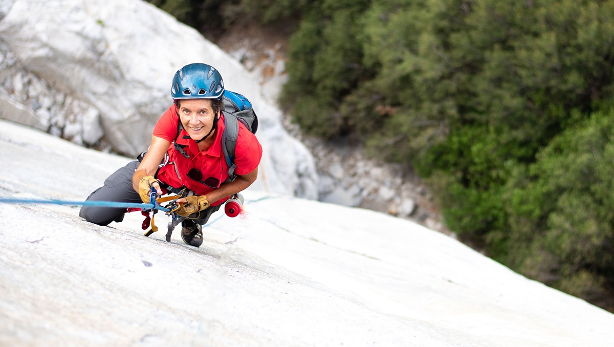 A photo of 70-year-old climber Dierdre Wolownick climbing a sheer rock face with a helmet and climbing gear