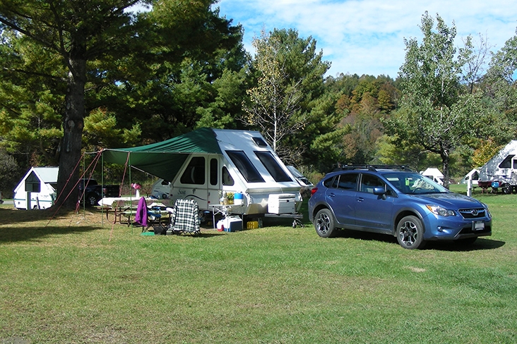 Christopher Corbett’s blue 2014 Crosstrek and an Aline camper tucked nicely in a grassy open campsite with a few trees for shade.