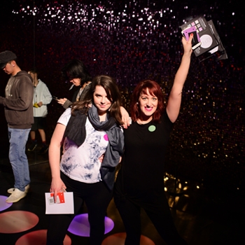 The author and Drive’s art director, both white women, pose mid-dance move in a dark room with multi-colored circle lights on the floor.