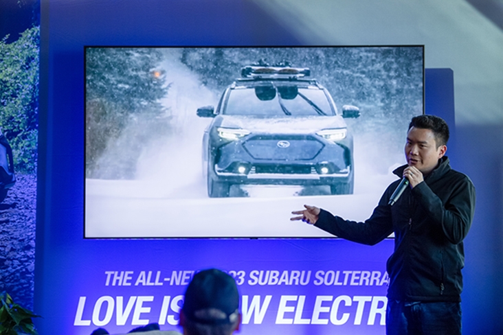 Garrick Goh, Subaru Solterra Carline Planning Manager, stands in front of a screen as he gives a presentation. On the screen is a Subaru Solterra and below the vehicle it says, The all-new 2023 Subaru Soltera. Love is now electric.