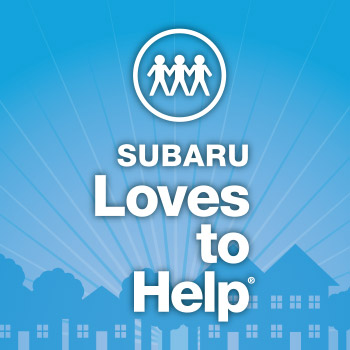 Subaru Loves to Help logo. It says, Subaru Loves to Help in white lettering. In the background, various houses are illustrated. The background is a soft blue color, and the houses are a darker blue with white windows and doors.