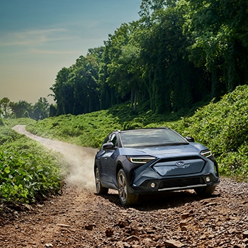 A 2023 Subaru Solterra cruises through a dusty, rocky path surrounded by greenery.
