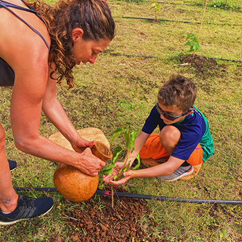 Writer Michele Bigley is holding a vase of water, and she’s helping to water a newly planted tree that her son Nikko is supporting with cupped hands.