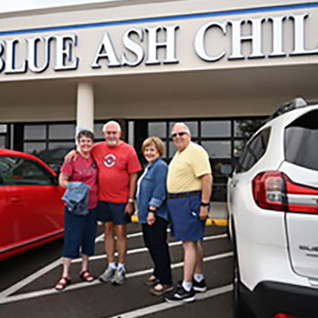 The two married couples are standing in a parking lot in front of the Blue Ash Chili building. They are next to the Subaru Ascent Touring, and Blue Ash Chili stands out in large white lettering on the building.