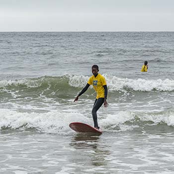  Instructor Farmy Dia rides a wave with confidence wearing a yellow Laru Beya Collective T-shirt and black athletic shorts. 