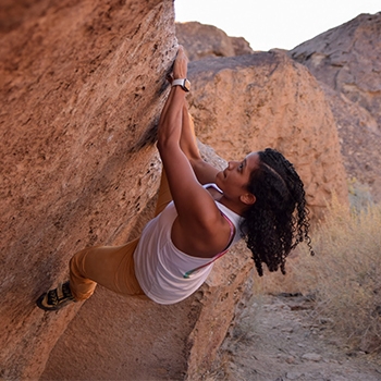 Indira Orozco free climbs a steep, reddish-colored rock face.