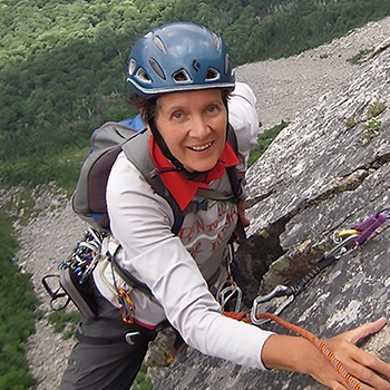 Dierdre Wolownick, wearing a helmet and smiling as she climbs up a steep rockface.