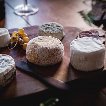 A variety of artisan cheeses on cutting boards with grapes and sliced sausages surrounding them.