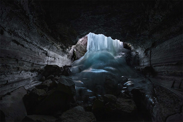 A frozen waterfall in a cavern with an explorer gazing up in wonder.