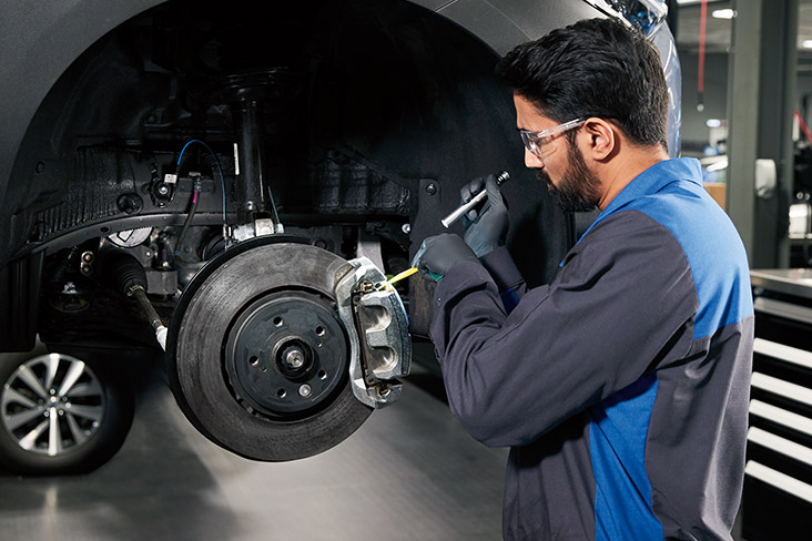 A Subaru service technician performing a brake pad and rotor inspection on a vehicle. 