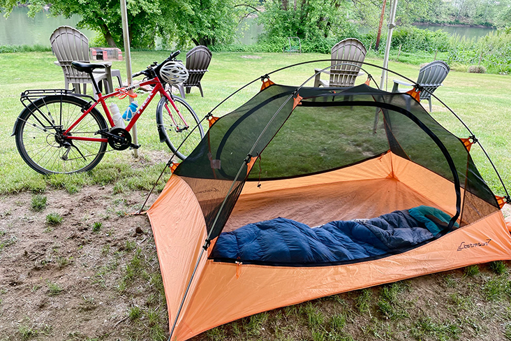 A small orange tent set up in a grassy field with the author's bike nearby.