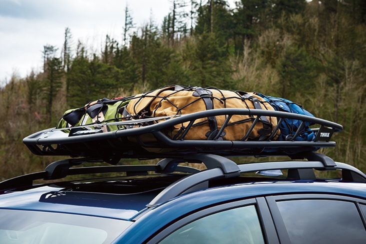 Closeup of a roof cargo basket that is filled with packed bags and is on top of a vehicle crossbar set.