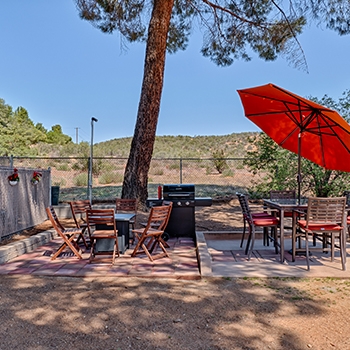 Two patio sets under a tree, one with a red umbrella. Mountains are in the background.