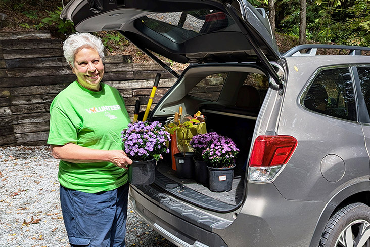 Patty Mallicote is standing behind her Subaru Forester, and she is holding a plant in a pot. The back of the Forester is filled with other pots of plants for Tallulah Gorge State Park in Georgia.