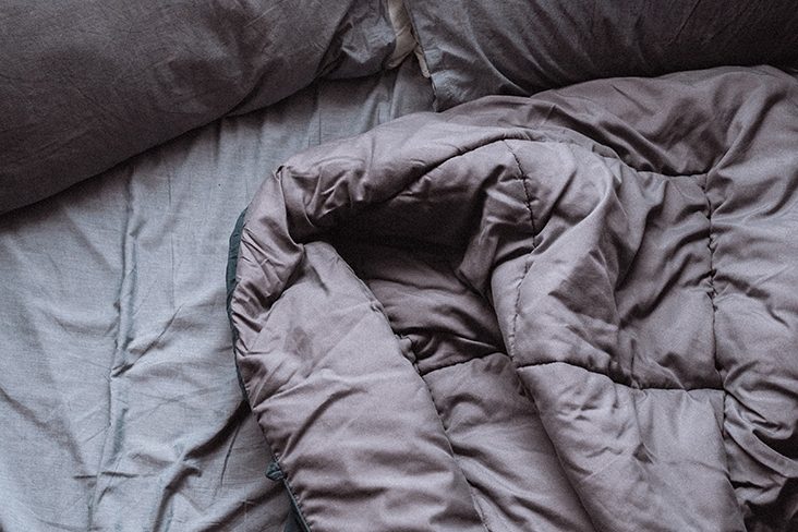 Disheveled gray bedding with a window providing daylight that is shining in