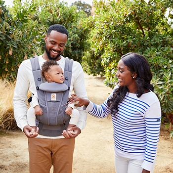Walking down a dirt path, father is wearing the baby carrier with his baby facing outward with a mother touching the baby's hand