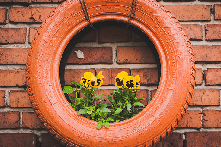 A tire is hung like a piece of artwork against a brick wall. The tire is painted  orange and has yellow pansies planted inside of it.