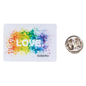 A rectangular metal pin with a white background shows an explosion of rainbow colors with the words “LOVE” inside. In the lower right-hand corner it says, “SUBARU” in capital letters.