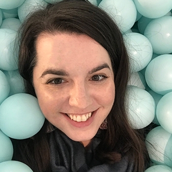 A close-up photo of the author, a white woman with brown hair, smiling surrounded by pale blue plastic balls in a ball pit.