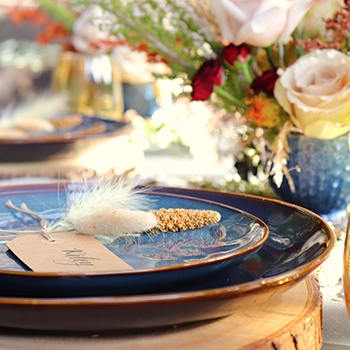 Blue dinner plates with place cards on top and a floral arrangement next to them.