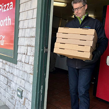 Jack Frost is leaving a pizza place with five boxes of pizza stacked in his arms for Ellsworth educators.