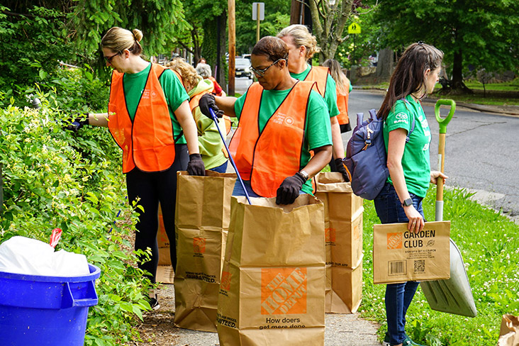 Subaru employees are helping to cleanup trash in the city of Camden, New Jersey. They're wearing Subaru Loves the Earth T-shirts and orange vests and are carrying bags for the waste.