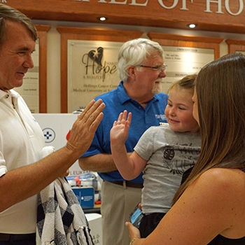 H. R. Hicks is high-fiving a child who’s in the arms of a female, who could be his mother.