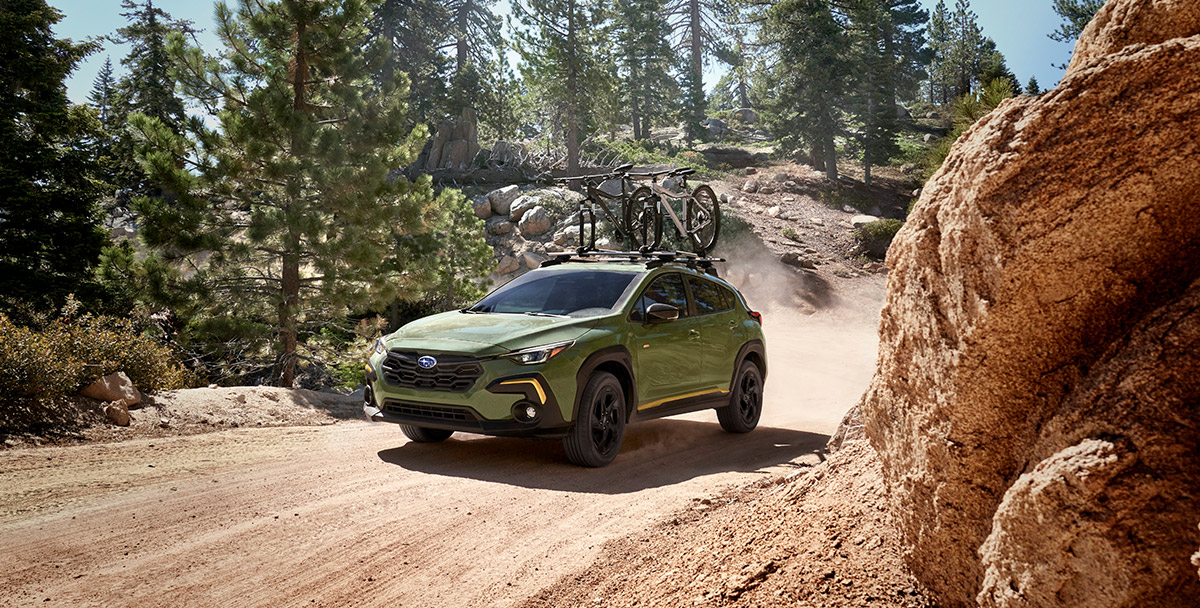A green 2024 Subaru Crosstrek carrying bikes travels through a dirt road in a forest.