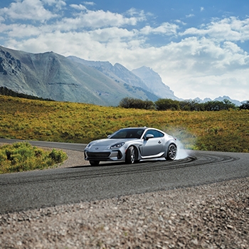 A 2022 Subaru BRZ in Ice Silver Metallic takes a sharp corner, kicking up dust. Mountains are in the background.