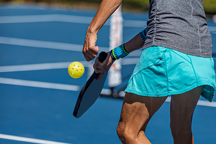 A close-up of a pickleball racket and wiffle ball being hit by a pickleball player on a court.
