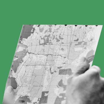 A black-and-white image of a hand holding a paper map on a green background