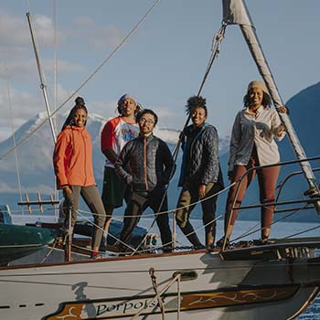 A group of CTT members stand smiling on a large sailing vessel with ice-capped mountains in the background.